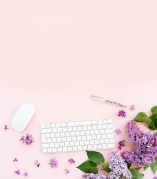 Flat lay top view home office workspace - modern keyboard with lilac flowers, copy space on pink background. Top view home office workspace