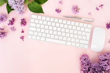 Flat lay top view home office workspace - modern keyboard with lilac flowers on pink desk background. Top view home office workspace