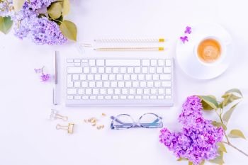 Flat lay top view home office workspace - modern keyboard with lilac flowers on white background. Top view home office workspace