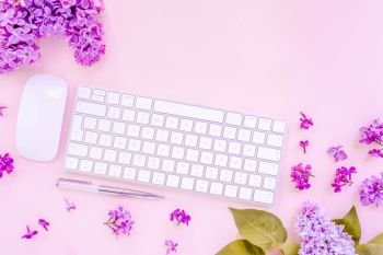 Flat lay top view home office workspace - modern keyboard with lilac flowers on pink desk background, toned. Top view home office workspace