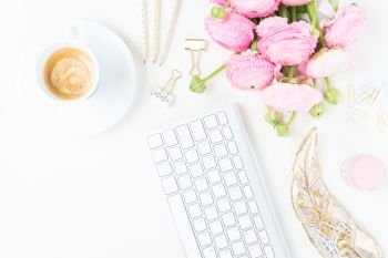 Flat lay home office workspace - modern keyboard with cup of coffee and pink ranunculus flowers. Top view home office workspace