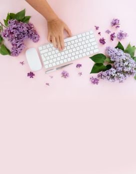 Flat lay home office workspace - modern keyboard with someone hand typing, fresh lilac flowers. Top view home office workspace