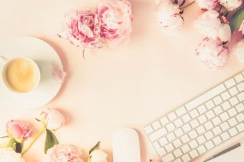 Flat lay home office workspace frame - modern keyboard with female accessories and fresh peony flowers, copy space on pink background, toned. Top view home office workspace