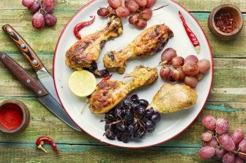 Baked chicken legs with grapes on rustic wooden table. Grilled spicy chicken legs