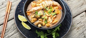 Spicy thai soup tom yam in plate on rustic wooden background. Thai tom yum soup with shrimp