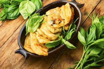 Pie stuffed with spring greens and cheese. Homemade qutabs or kutab. Azeyrbajan food.Flat lay. Tasty Azerbaijani qutab with young greens,wooden table