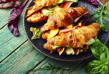 Croissant or sandwich,morning food.Croissants with trout, meat bacon, vegetables and fruits. Croissant with salted filling on a plate