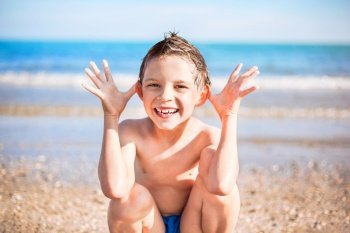 smiling boy with hands close to the head sitting on the beach. smiling boy sitting on the beach