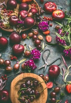 Summer fruits and berries still life on dark rustic background with wooden bowls and garden flowers, top view