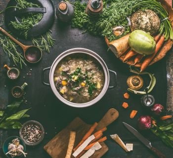 Beef and cabbage soup or stew in cast iron cooking pot on dark background with low carb vegetables, spices ingredients and wooden spoon, top view. Healthy clean low-calorie food and eating concept