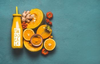 Bottle with healthy energetic drink and word smoothie, for cold season with orange ingredients : pumpkin, persimmon , orange fruits, ginger and turmeric or curcuma powder , top view