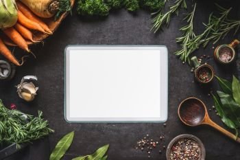 Food cooking and healthy eating background with  tablet pc with empty white screen. Fresh seasoning, spoon and vegetables ingredients, top view. Copy space for your text and design