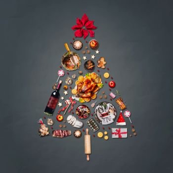 Christmas tree made with various Christmas food: turkey on platter, roasted ham, sweets and candies, cookies , mulled wine, gingerbread  man decorated with gift box and poinsettia on gray background