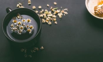Cup of herbal chamomile tea with  dried chamomile flowers and honey on dark background, top view. Remedy to treat a wide range of health issues. Herbal medicine concept. Healing herbs.