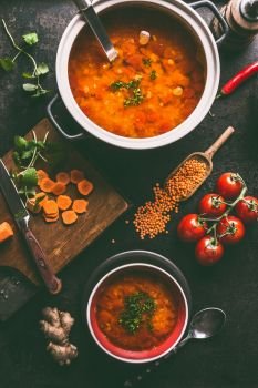 Lentil soup in pot and bowl with spoon and ladle. Cooking ingredients on dark rustic kitchen table background, top view. Healthy vegan food concept. Vegetarian lentil meal dishes. Clean eating.