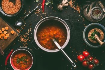 Healthy vegan lentil soup in cooking pot with ladle on dark kitchen table background with ingredients. Vegetarian food. Clean diet eating. Source of plant based protein