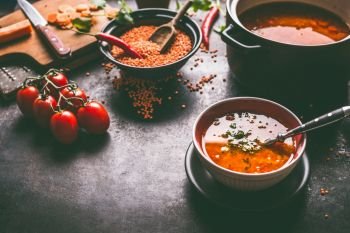 Healthy vegan lentil soup in bowl with spoon on dark kitchen table background with ingredients. Vegetarian food. Clean diet eating. Source of plant based protein