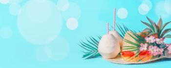 Beach accessories with fresh coconut, drinking straws and tropical leaves and flowers , sunglasses and straw hat on sunny blue background with bokeh. Summer holiday concept, banner.