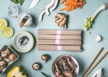 Asian food ingredients flat lay on light blue kitchen table background: noodles, vegetables,mushrooms and spices. Tasty vegan cooking and eating. Chinese or Thai cuisine. Healthy nutrition concept.