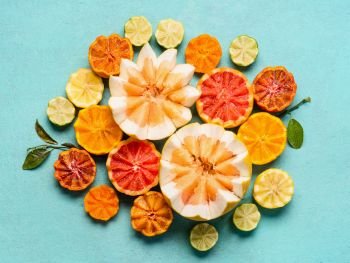 Various citrus fruits on light blue background, top view. Composing with half of orange fruits, lemon, grapefruit, mandarin, lime, clementines, pomelo and blood orange. Flat lay. Healthy food
