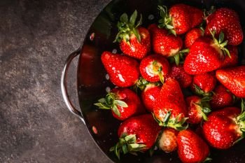 Close up of fresh strawberries in black colander bowl, top view