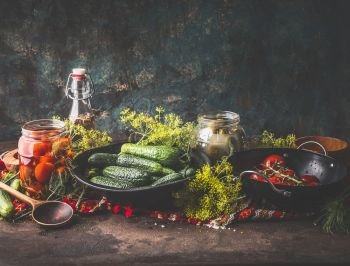 Still life with cucumber and tomatoes pickling, canning and preserving ingredients on rustic table at dark wall background. Healthy fermented food concept. Clean eating. Harvest storing