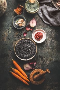 Black lentils with cooking ingredients for tasty vegan dishes on dark background. Top view. Healthy vegetarian eating concept. Horizontal banner. Plant based protein source. Top view