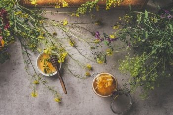 Natural honey in different jars with honey spoon and wild flowers on dark concrete background. Natural and healthy food concept. Top view