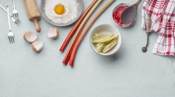 Baking preparation with rhubarb, egg yolk, flour, egg shell, wooden rolling pin, dish cloth and forks on light kitchen table. Top view with copy space