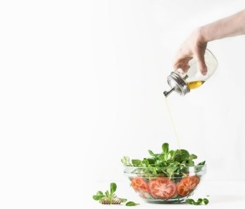 Woman hand pouring  oil over big bowl with salad. Lunch making with fresh green  lettuce,tomatoes and olive oil at white background. Healthy food.