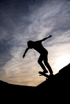 Silhouette of a Skater riding the skate in a half pipe in a skate park against dramatic hazzy sky
