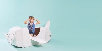 Little cute girl playing with a cardboard airplane. White retro style cardboard airplane on mint green background . Childhood dream imagination concept . Horizontal format .