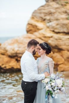same couple with a bride in a blue dress walk along the ocean shore