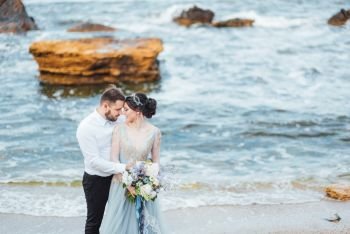 same couple with a bride in a blue dress walk along the ocean shore