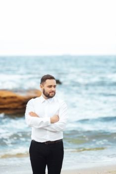 the groom in a white shirt and black pants stands on the beach