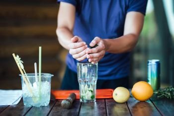 Barman prepares fruit alcohol cocktail based on lime, mint, orange, soda and alcohol