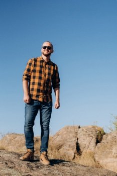 bald guy with a beard in jeans warm shirt and trekking shoes on granite rocks