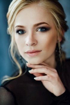Blonde girl with blue eyes in a black dress in a dark turquoise interior
