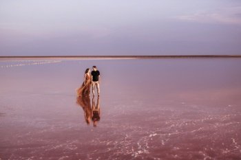 girl and a guy on the shore of a pink salt lake at sunset