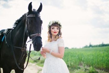 girl with red lips in a white dress near a black horse