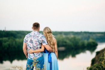 blonde girl with loose hair in a light blue dress and a guy in the light of sunset in nature