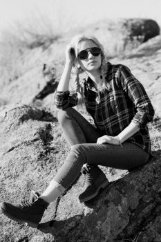 blonde girl with pigtails in a shirt, jeans, red shoes and black glasses on granite rocks