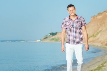 guy in white trousers walks along the seashore against the backdrop of clay slopes