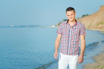 guy in white trousers walks along the seashore against the backdrop of clay slopes