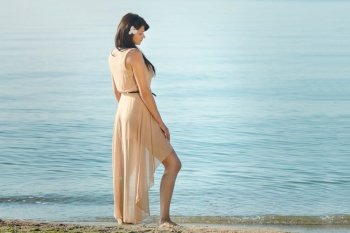 girl with black hair in a beige dress on the shore of the blue sea