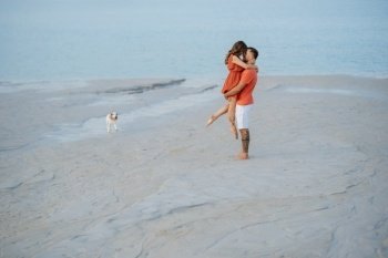 young couple in orange clothes with dog on an empty sandy beach