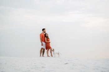 young couple in orange clothes with dog in the desert white sands
