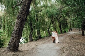 a guy and a girl are walking along the banks of a wild river overgrown with willows and forest
