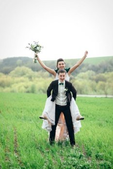 the groom in a brown suit and the bride in an ivory-colored dress on a green field receding into the distance against the sky