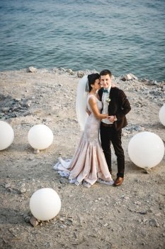 the groom in a brown suit and the bride in an ivory dress on the rocky seashore